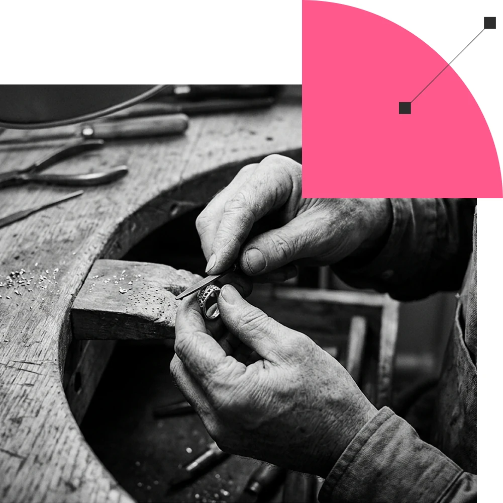 Mãos de um artesão lapidando um anel, em preto e branco, com uma forma rosa aplicada sobre a imagem
